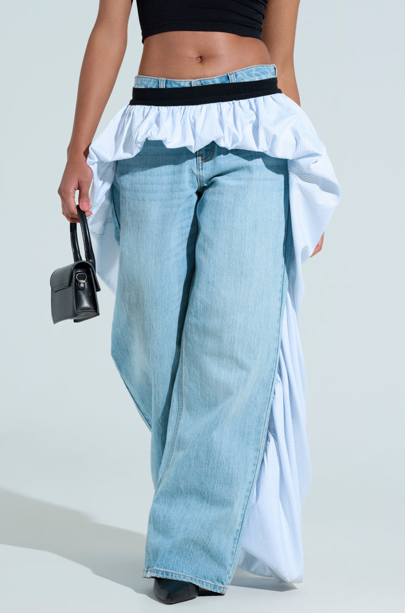 A model showcases the RUNWAY BELT SKIRT, a stylish light-blue wide-leg piece with ruffled waist details and an asymmetrical high-low cut. Paired with a black crop top and a chic small black handbag, it creates a high-fashion look against the plain white background.