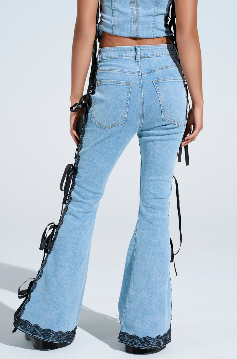 A person poses against a plain backdrop wearing TICKED AND TIED LACE AND BOW DETAIL DENIM PANTS in light blue with lace-up panels, paired with a matching denim top.