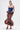 A woman poses in a strapless royal blue corset top with an adjustable lace-up back and the high-waisted LADY LUX BROCADE BUBBLE HEM MIDI SKIRT, featuring an orange and blue floral pattern. She completes the look with earrings and heeled sandals.