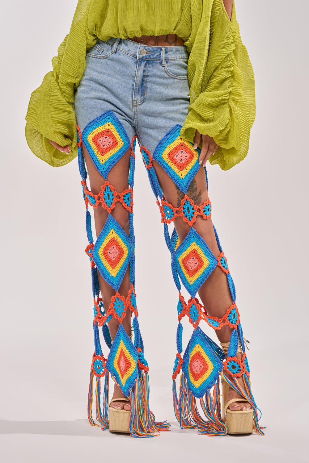 Wearing the OUT OF OFFICE CROCHET DENIM JEANS with diamond and floral crochet patterns in blue, orange, yellow, and red makes for a vibrant festival look—especially when styled with a green textured top and platform sandals. 0