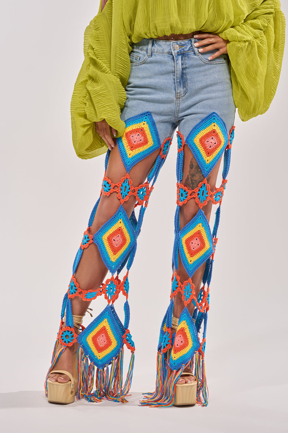 Someone sporting the OUT OF OFFICE CROCHET DENIM JEANS, featuring light blue crochet, colorful panels, and rope accents, teamed with a lime green textured top and beige platform sandals—a standout festival look. 1