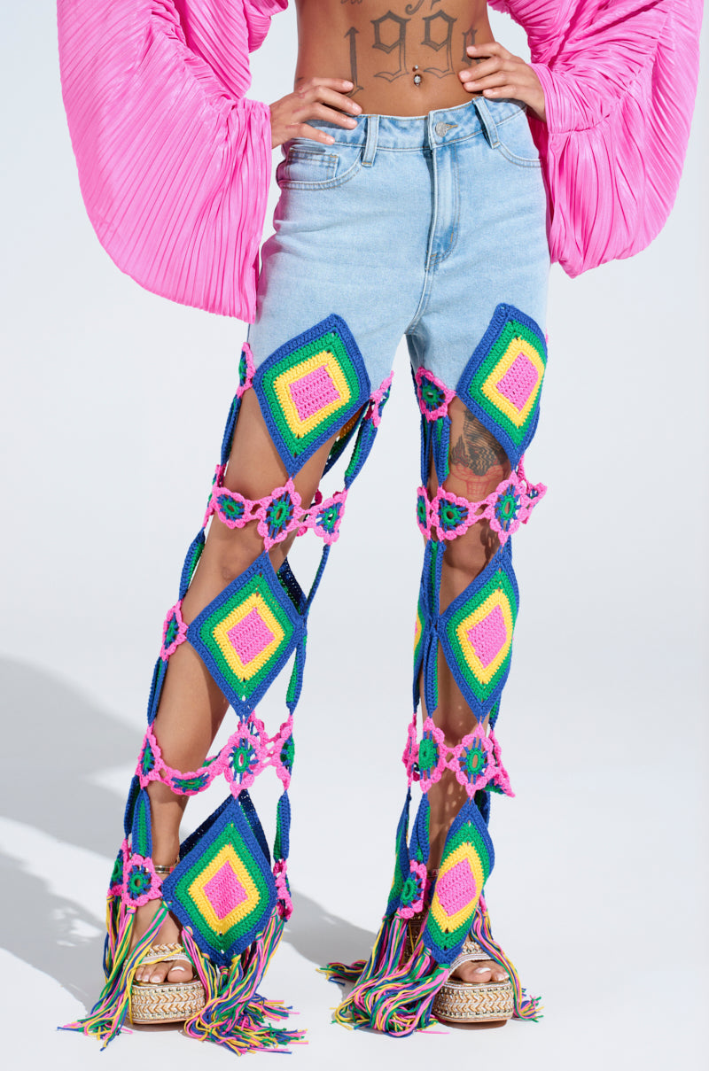 Someone sports colorful crochet leg coverings inspired by granny square motifs, showcasing geometric patterns in blue, pink, green, and yellow on OUT OF OFFICE CROCHET DENIM JEANS. The look is finished with platform sandals and a glimpse of a pink pleated top.