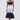 A woman wears the LOST IN THE CITY LAYERED POPLIN MIDI DRESS, designed with dark and light blue striped panels, a white waistband, and a voluminous dark skirt. She completes the look with a small white bag and white heeled sandals.