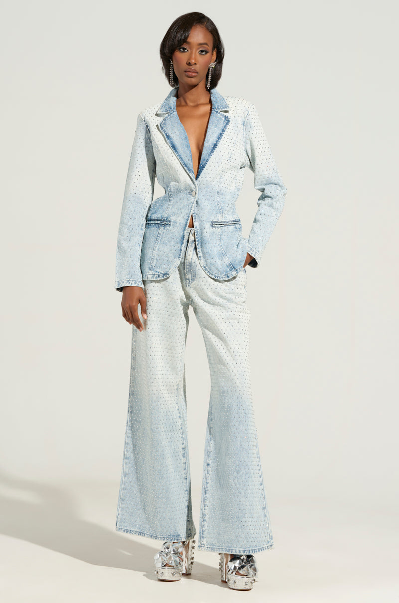 A person wearing an Electric Embellished Denim Blazer with flared pants stands against a light background in business casual style. They have one hand in their pocket and are sporting platform shoes.