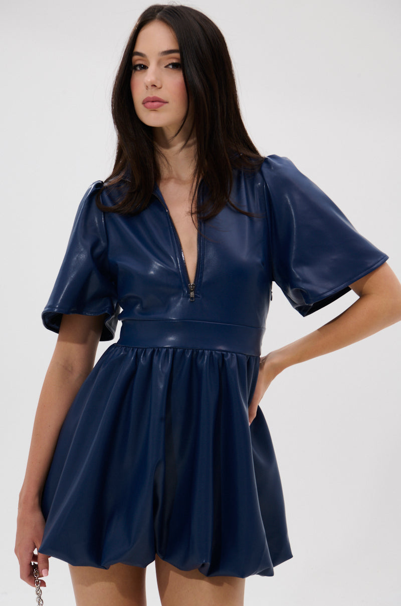 A woman with long dark hair models the LALA LOVE YOU PU MINI DRESS IN NAVY, featuring a zippered V-neck and flared skirt, against a plain light background.