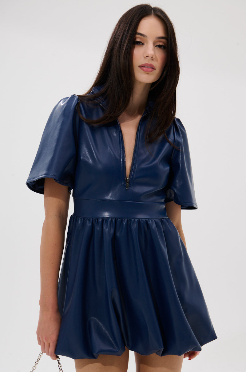 A woman wears the LALA LOVE YOU PU MINI DRESS IN NAVY, a faux leather fit-and-flare mini with puffed short sleeves and a front zipper, standing against a plain white background and looking at the camera.