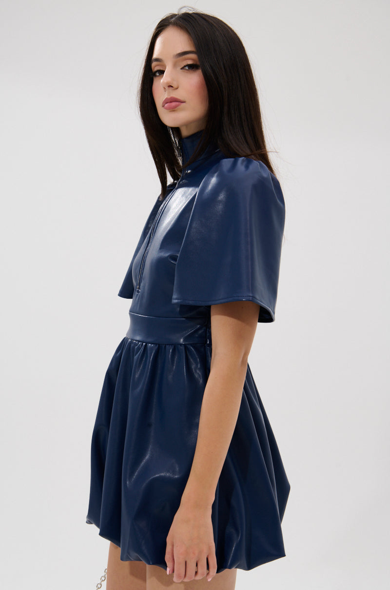 A woman with long dark hair wears the LALA LOVE YOU PU MINI DRESS IN NAVY, featuring a high collar and cape-like sleeves, as she stands against a light background and looks confidently at the camera.