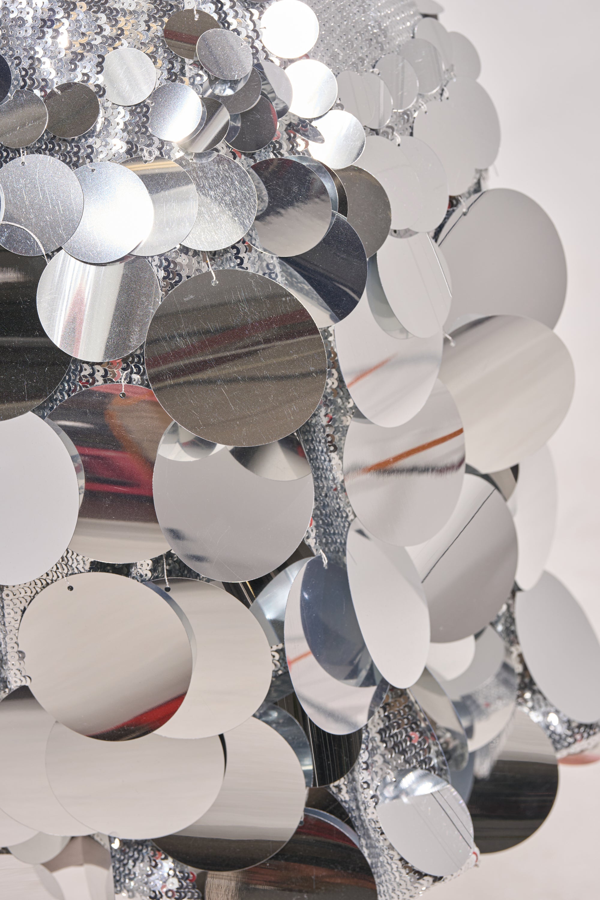 Close-up of overlapping, shiny silver discs on the LIFE OF THE PARTY SEQUIN MIDI DRESS IN SILVER, reflecting light and creating a textured, mirrored effect against a plain light background. 5