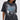 A woman in large black sunglasses and the KNOCK YOURSELF OUT DISTRESSED TEE, featuring chain and safety pin details, ripped shoulders, and a bold blue-and-white graphic. Her straight hair and confident look complete the grungy-chic vibe.