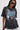 A woman in large black sunglasses and the KNOCK YOURSELF OUT DISTRESSED TEE, featuring chain and safety pin details, ripped shoulders, and a bold blue-and-white graphic. Her straight hair and confident look complete the grungy-chic vibe.