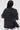 Person with long straight hair, seen from behind, wears the KNOCK YOURSELF OUT DISTRESSED TEE with rips and safety pins for a grungy-chic look. They carry a black shoulder bag with metal details and wear light blue jeans.
