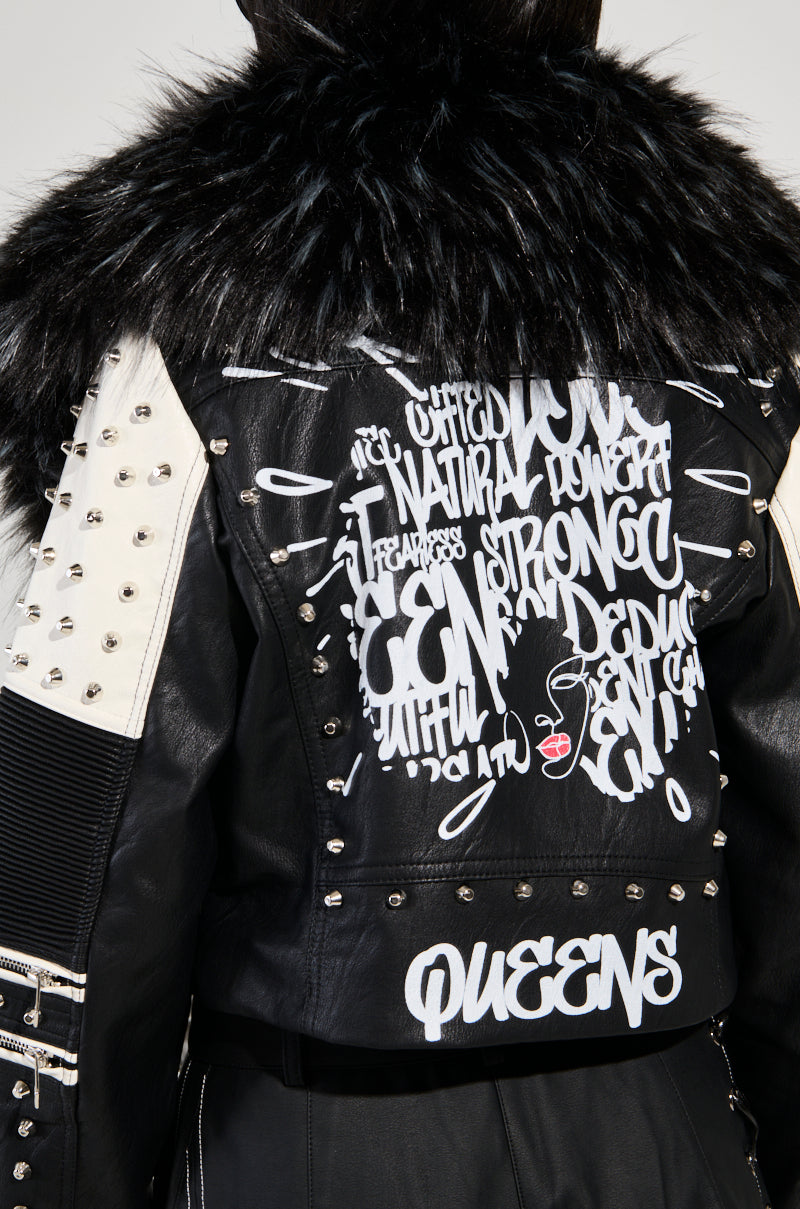 Dressed in the FROM THE BRONX FUR TRIM MOTO jacket, a person showcases streetwear style with its black faux leather design and a bold fur collar. The jacket's back is adorned with graffiti-style white lettering and red graphics, featuring words like "QUEENS," while the sleeves are embellished with edgy metal studs.