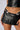 Close-up of a person's midsection wearing the TIME TO LOSE CONTROL MINI SKIRT, a club-ready black pleated mini skirt with a zipper detail, paired with a matching black faux leather top. The person has a belly button piercing and is showing a portion of a tattoo near their waist.