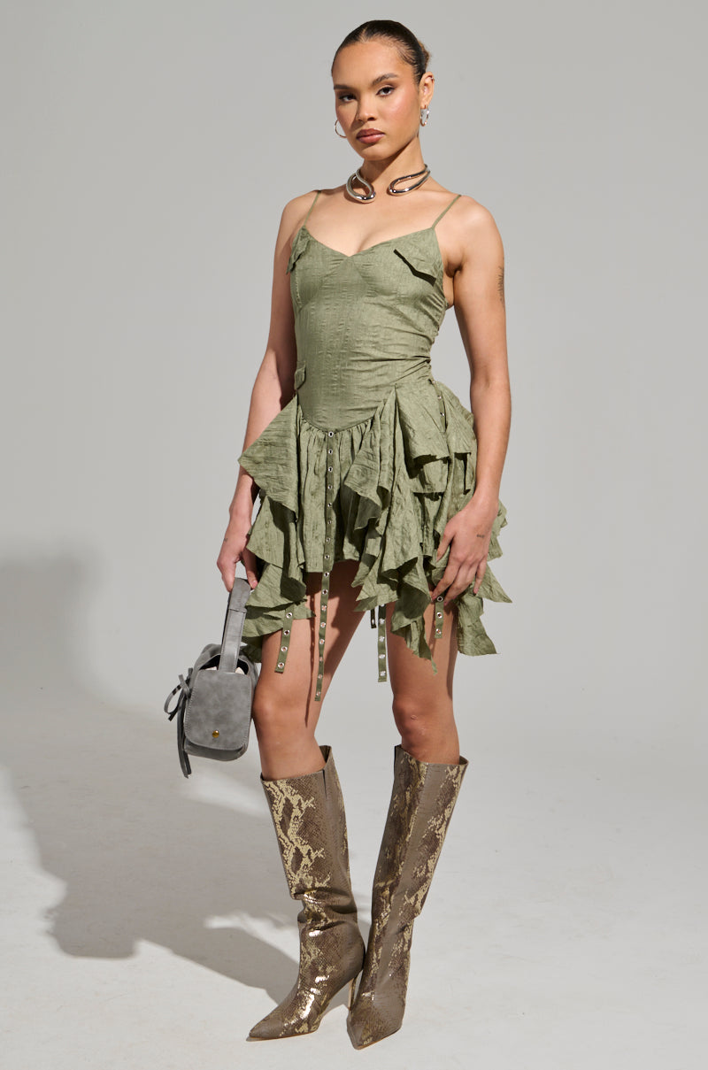 A vibrant CANT COMPARE CHIFFON MINI DRESS with spaghetti straps, complemented by a chunky necklace and a gray handbag, is paired with knee-high snakeskin boots. The ensemble strikes a pose against a plain background.