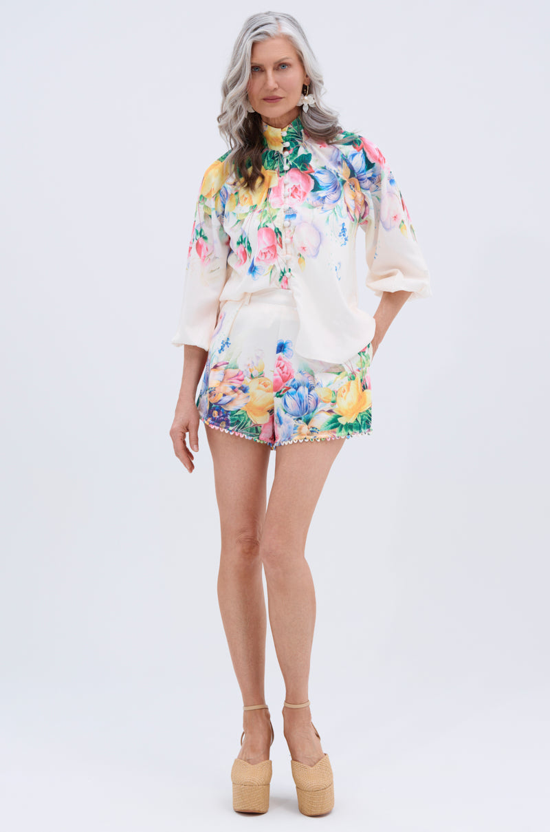 A woman with long gray hair wears the ROSE FLORAL BUTTON DOWN and matching floral shorts with platform sandals, standing against a plain white background.