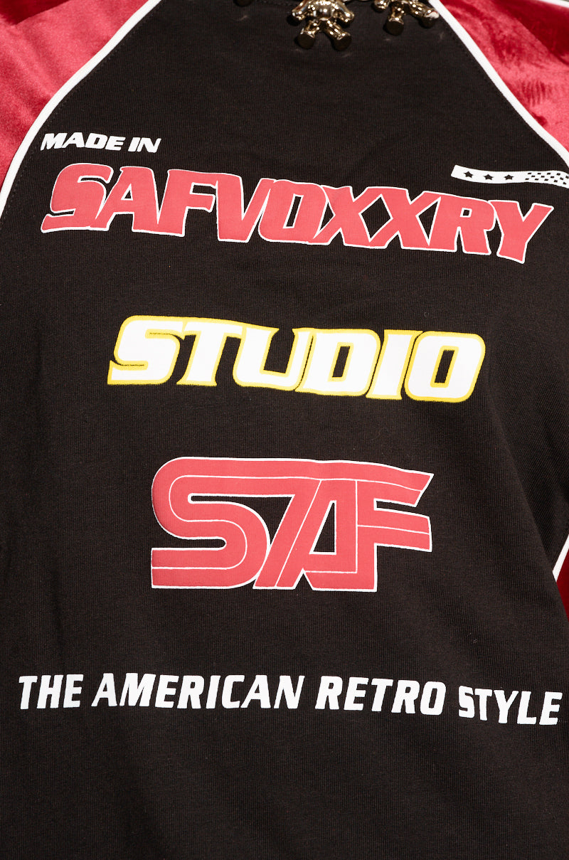 A close-up of THE AMERICAN JERSEY, a black shirt featuring bold red and yellow text that reads "MADE IN SAFVOXXRY," "STUDIO," and "STF." The bottom showcases the phrase "THE AMERICAN RETRO STYLE." With colorblock paneling in red and white design accents, this shirt infuses modern flair into classic cotton knit.