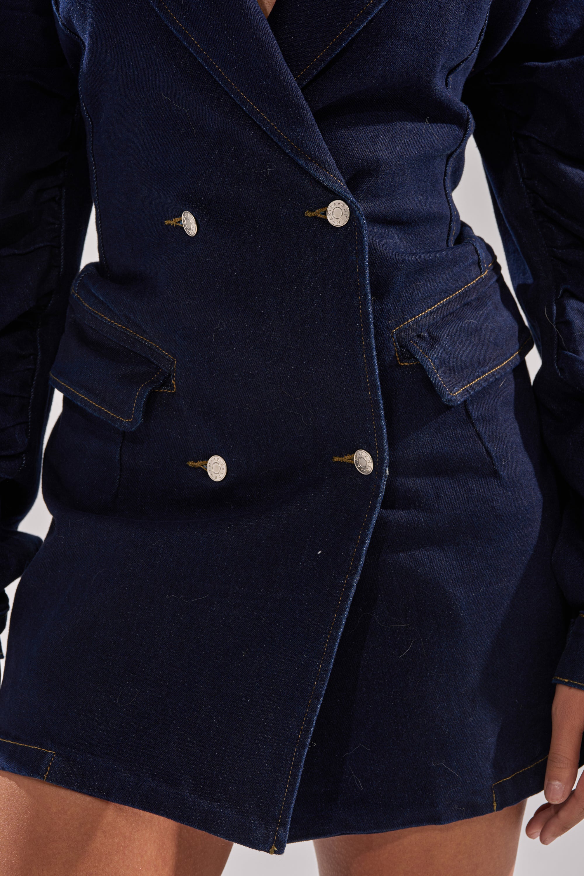 Close-up of a person wearing the BUSINESS MEETING CHIC BLAZER DRESS AND LEG WARMER SET IN DENIM, featuring a dark blue double-breasted style with silver buttons, flap pockets, and stitch detailing—a modern take on the power suit.