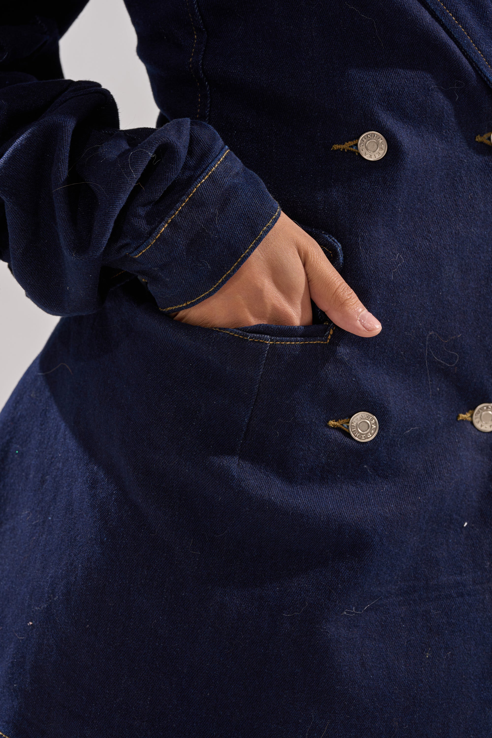 A hand is partly tucked into the pocket of the BUSINESS MEETING CHIC BLAZER DRESS AND LEG WARMER SET IN DENIM, featuring a dark blue wash, silver buttons, and visible yellow stitching.