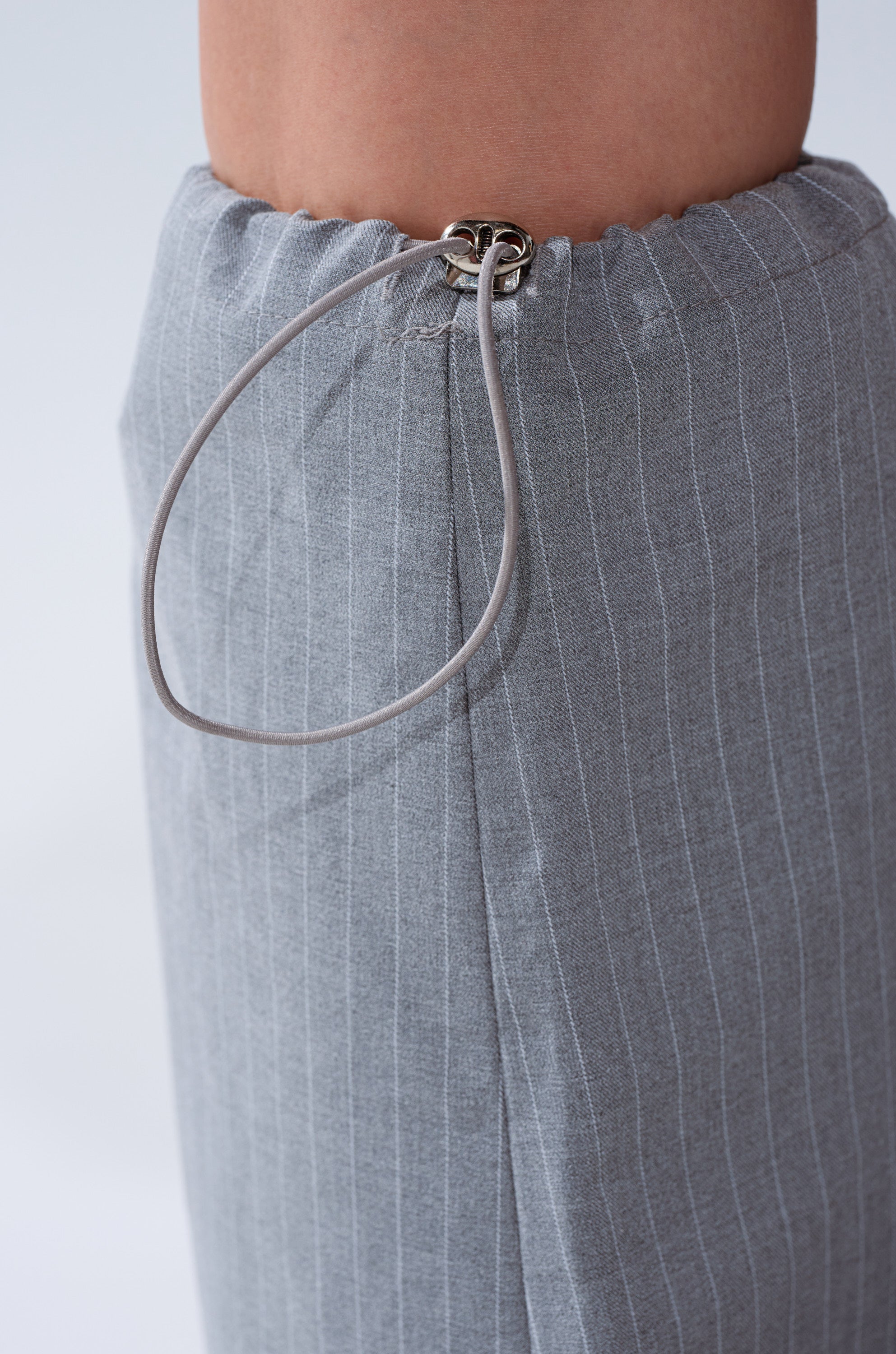 Close-up of the BUSINESS MEETING CHIC BLAZER DRESS AND LEG WARMER SET IN GREY, highlighting the gray pinstriped leg warmer with an adjustable elastic drawstring waistband secured by a metal fastener. 10