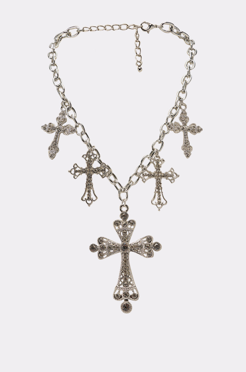 The STAY BLESSED NECKLACE is an oversized link chain with five ornate cross pendants—a large rhinestone cross at the center and four smaller crosses evenly spaced along the silver chain. 0