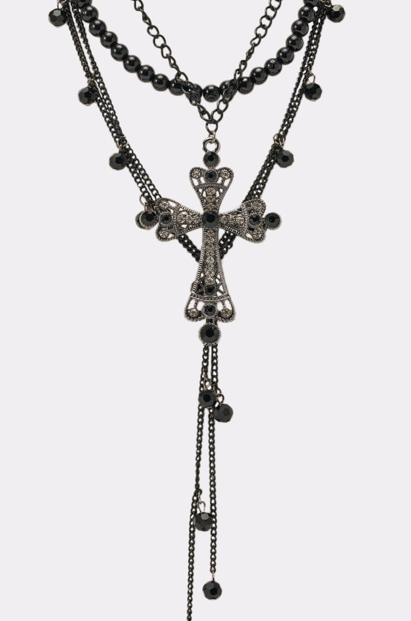 The TAKE CARE NECKLACE is a gothic statement piece with layered black beads, a large ornate cross pendant, black gemstones, and dangling chains embellished with small black beads. 3