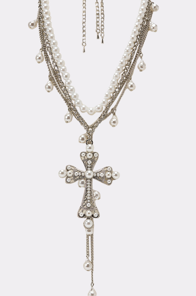 The PRINCESS PEARL NECKLACE features silver chains, pearl beads, and a striking pearl cross pendant with rhinestones. Displayed on a plain white background, it's the perfect layered accessory to elevate any outfit. 2