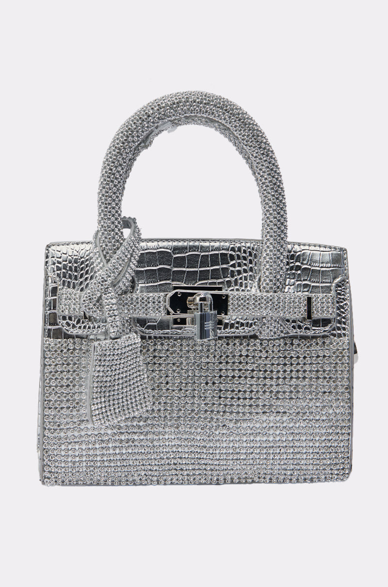 The SWERVE BLING PURSE is a stunning silver rhinestone bag with a crocodile-textured pattern, sparkling embellishments, top handle, front flap, and decorative lock buckle.