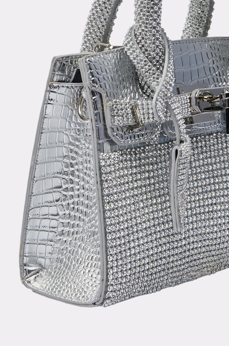 A close-up of the SWERVE BLING PURSE, featuring a shiny silver crocodile-texture pattern, sparkling rhinestones, silver hardware, sturdy handles, and a decorative lock detail.
