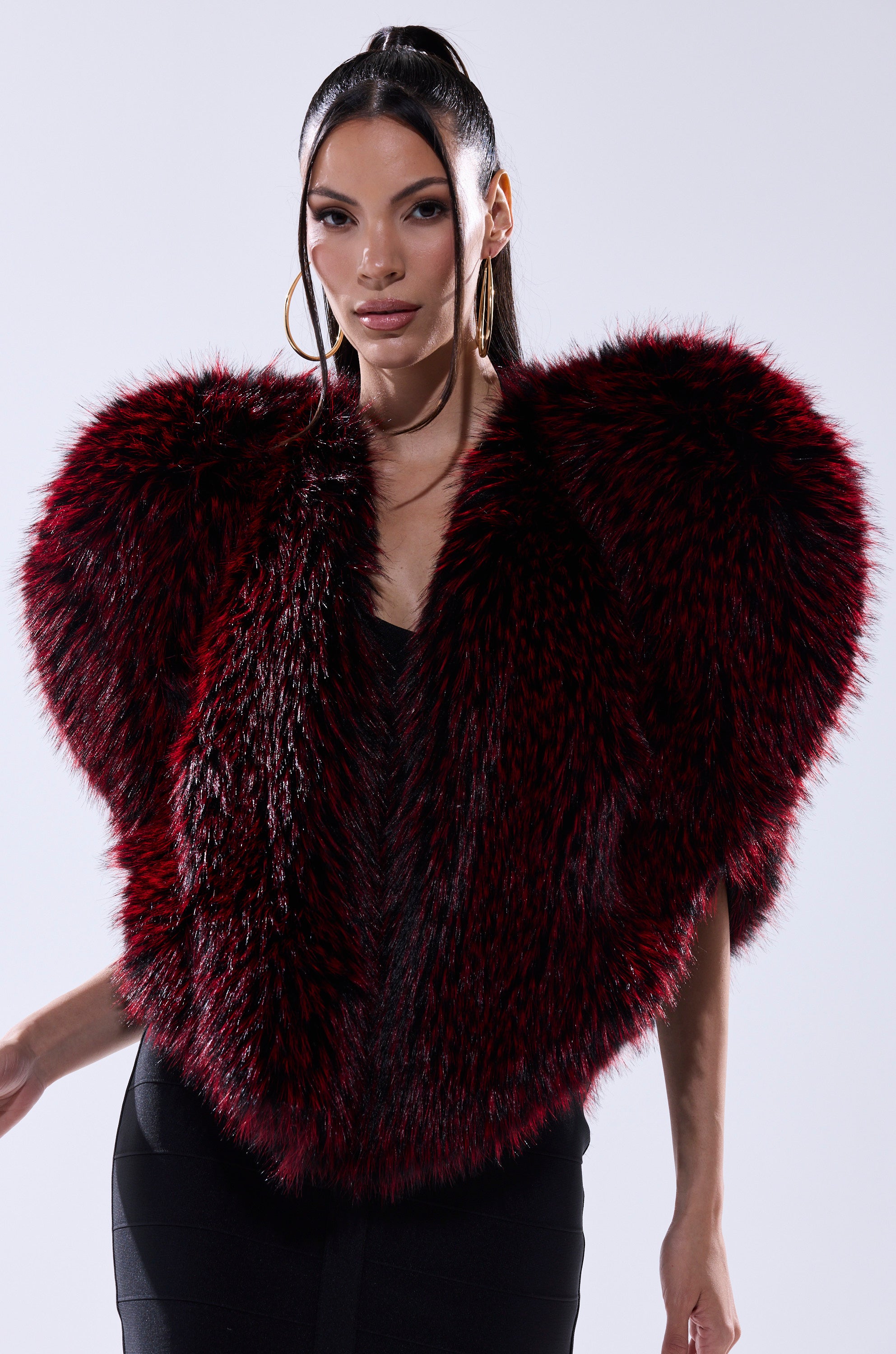A woman with long, dark hair wears large hoop earrings and the STAR CROSSED LOVER FAUX FUR VEST in deep red and black over a black dress, posing against a plain light background for a bold layered look.