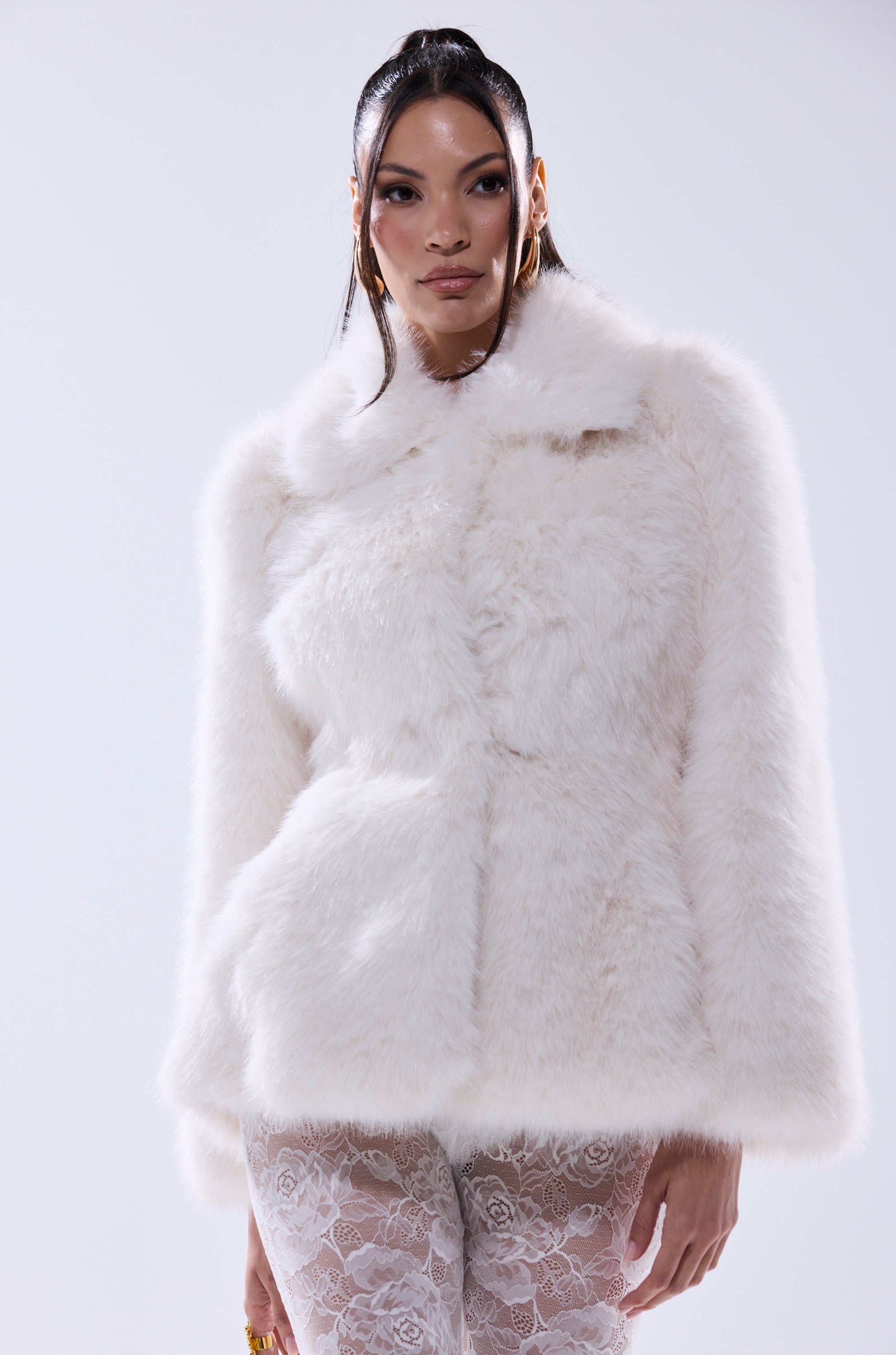A person with long dark hair wears the KENNY PEPLUM FAUX FUR jacket and white lace pants, standing against a plain light background.