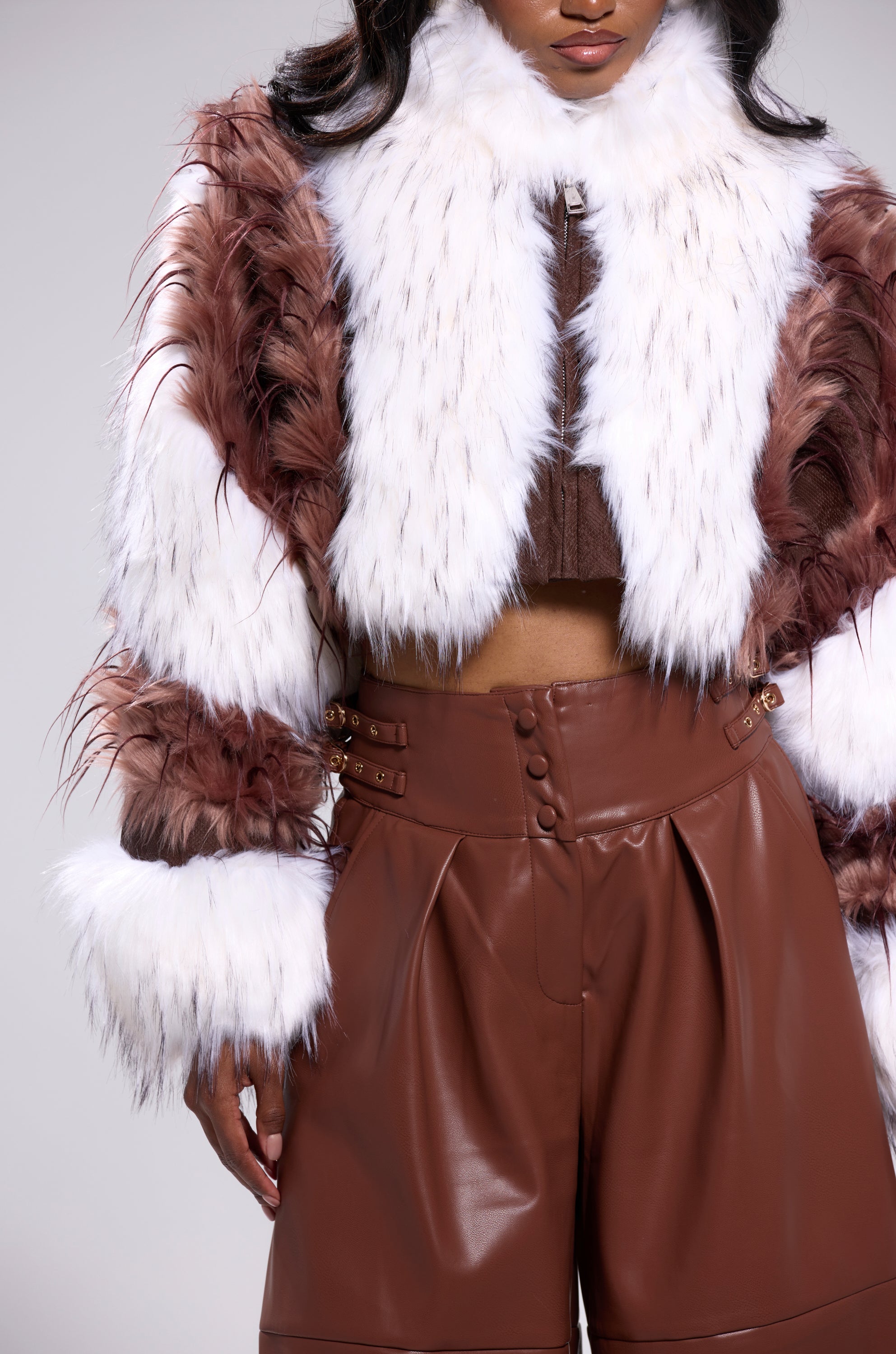 A woman wears high-waisted brown leather pants and the FRANKIE PATCHWORK FAUX FUR jacket in white and brown, featuring a wide white collar and cuffs. Her face is partially out of frame. 7