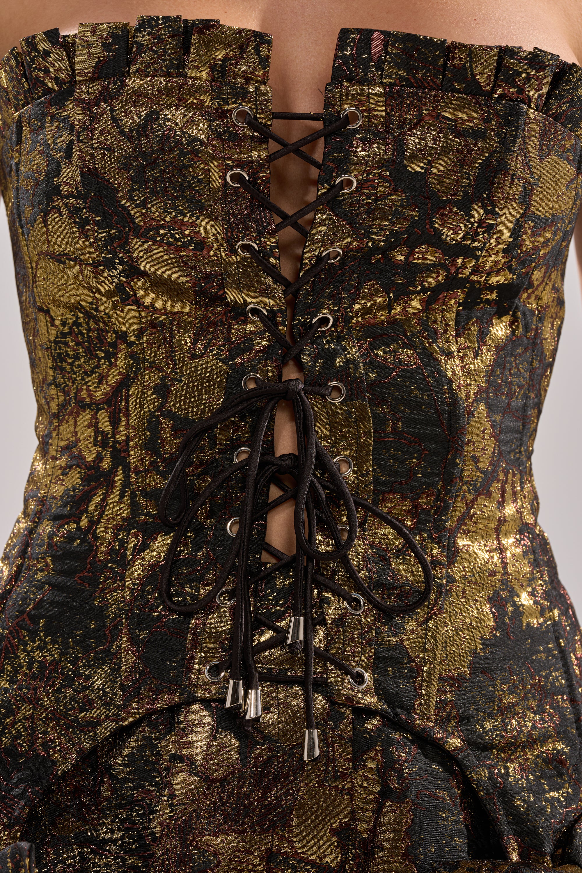 Close-up of the LOTUS BROCADE CORSET: gold-and-black floral design with black laces through metal eyelets, tied in a center bow. The strapless corset top features an intricate, textured brocade pattern.