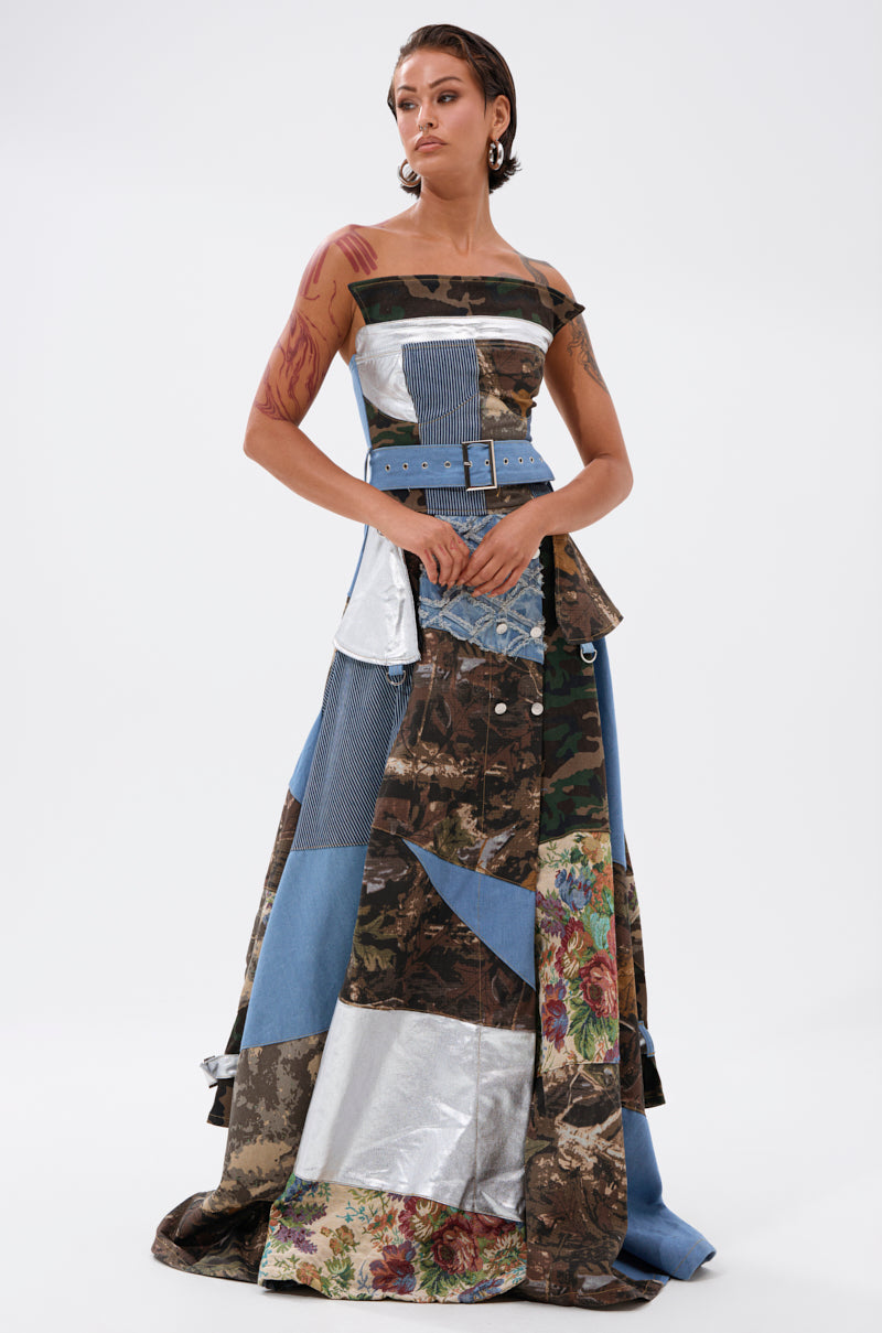 A woman exudes confidence in the STRAPLESS TRENCH MAXI DRESS WITH PATCHWORK DETAIL, featuring camouflage, denim, floral, and metallic silver fabrics with a wide blue belt—a true runway statement piece.