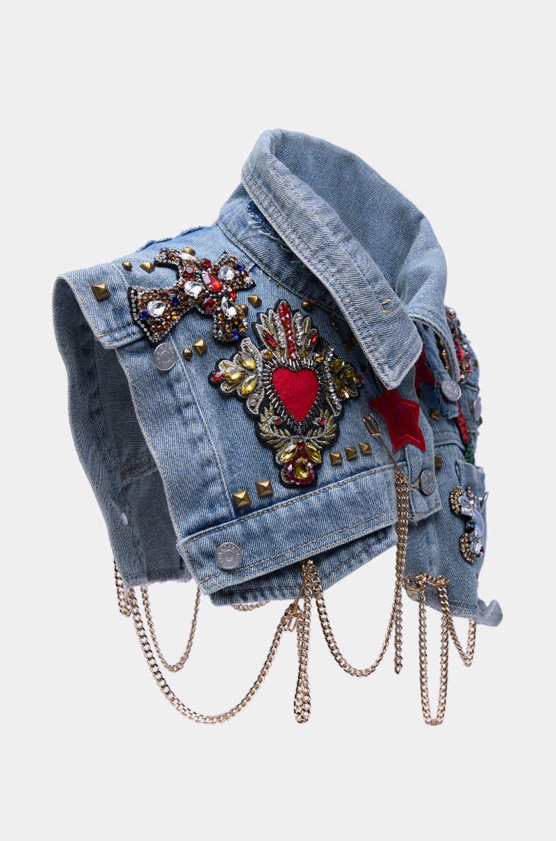 The STYLE ME UP DENIM COLLAR is a cropped light blue vest with colorful patches, beadwork, gold studs, red and gold heart motifs, red stars, and hanging gold chains—displayed on a plain white background.