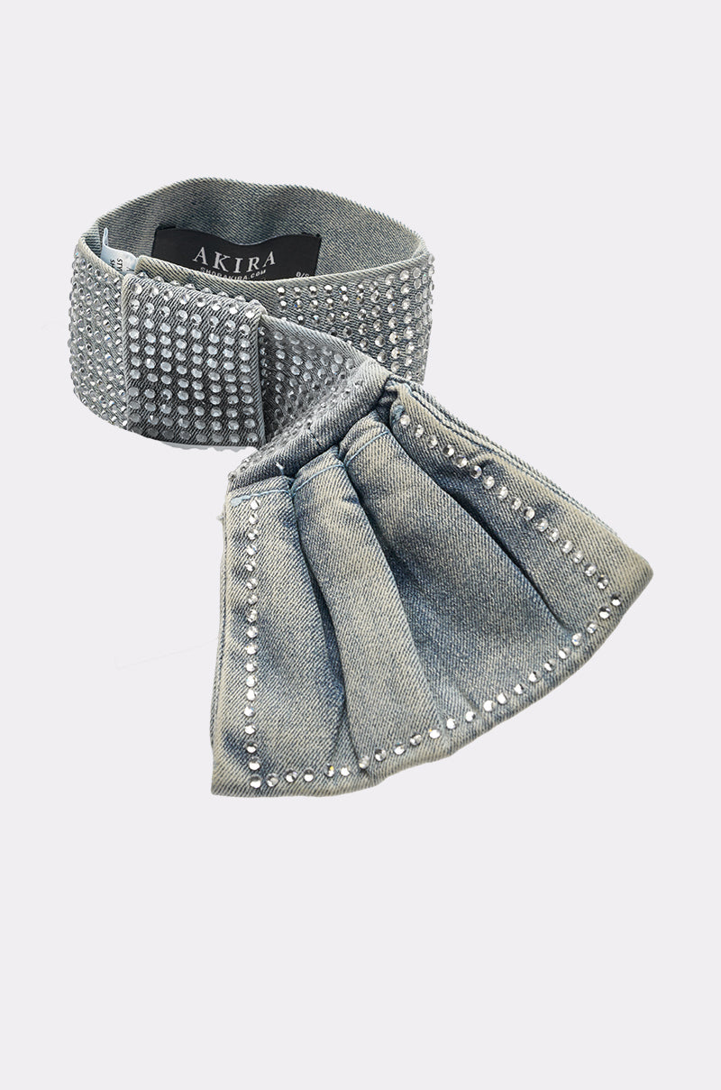 The WITH A BOW DENIM NECKLACE from AKIRA features silver studs, a wide denim band, and a large decorative bow—perfect for pairing with statement pieces. Photographed on a white background. 5