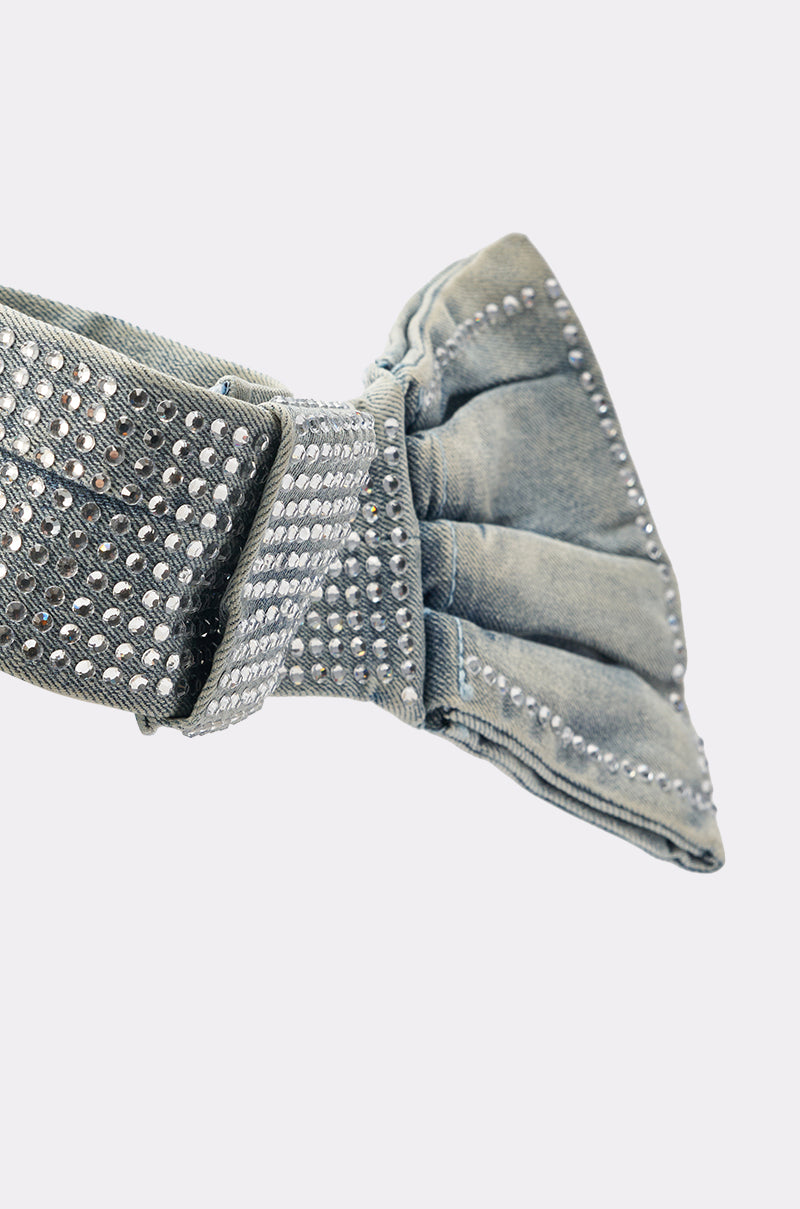 The WITH A BOW DENIM NECKLACE is shown in close-up, featuring a denim bow accented with rows of silver studs against a plain white background. 6