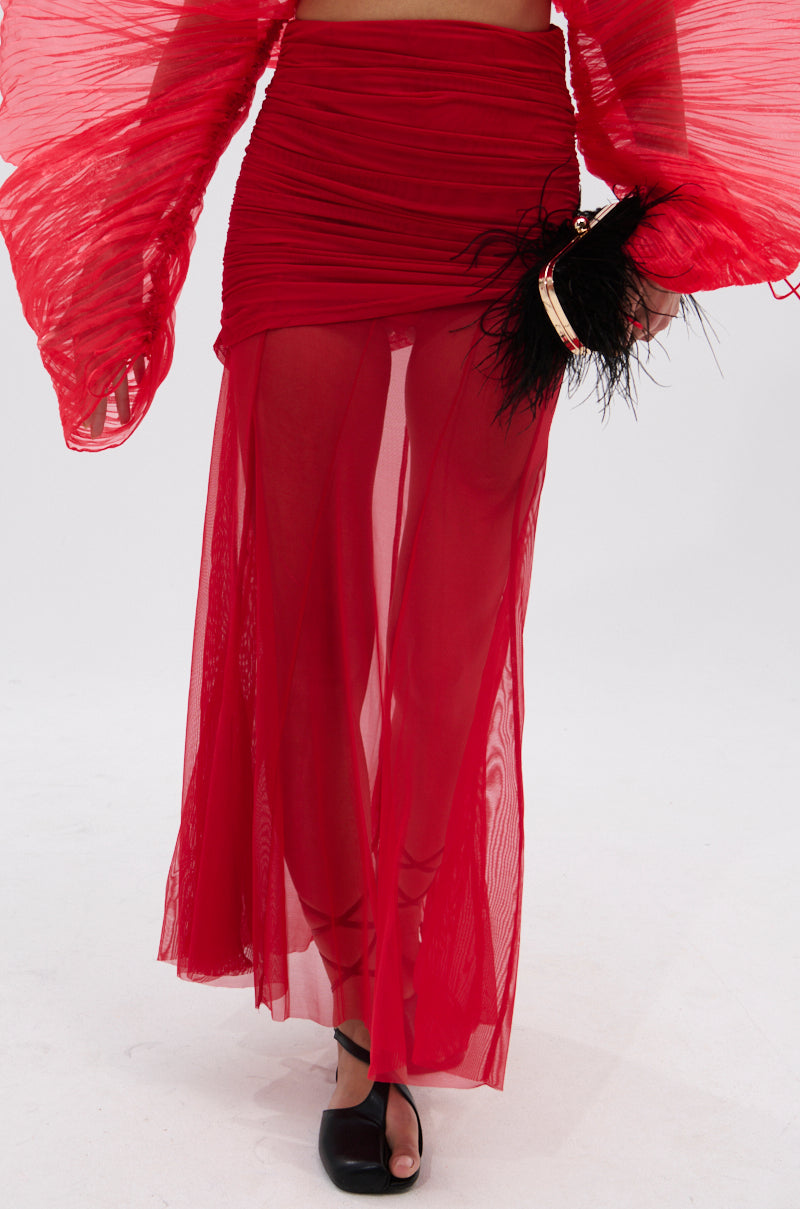 Wearing the EASY ENOUGH RED MESH MIDI SKIRT with ruched details and a matching top, this person holds a black feathered clutch and wears black open-toe shoes, posing against a plain white background. 2