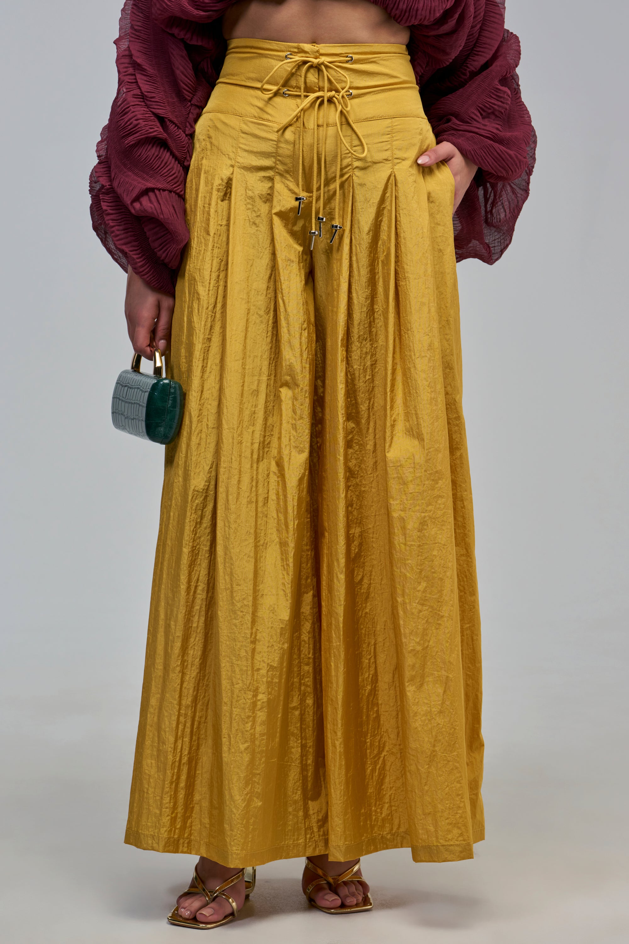 A person wearing mustard yellow DANCE THE NIGHT AWAY PALAZZO PANT with a drawstring waist and metallic gold strappy sandals.