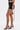 A woman stands sideways in the LOOK AT THIS ULTRA MINI SKIRT, paired with a matching crop top and black strappy high-heeled sandals with long wraparound ties. The background is plain white.