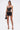 Woman wearing the LOOK AT THIS ULTRA MINI SKIRT, paired with a black strapless corset top, strappy high heels, choker necklace, and holding a small black handbag, standing against a plain white background.