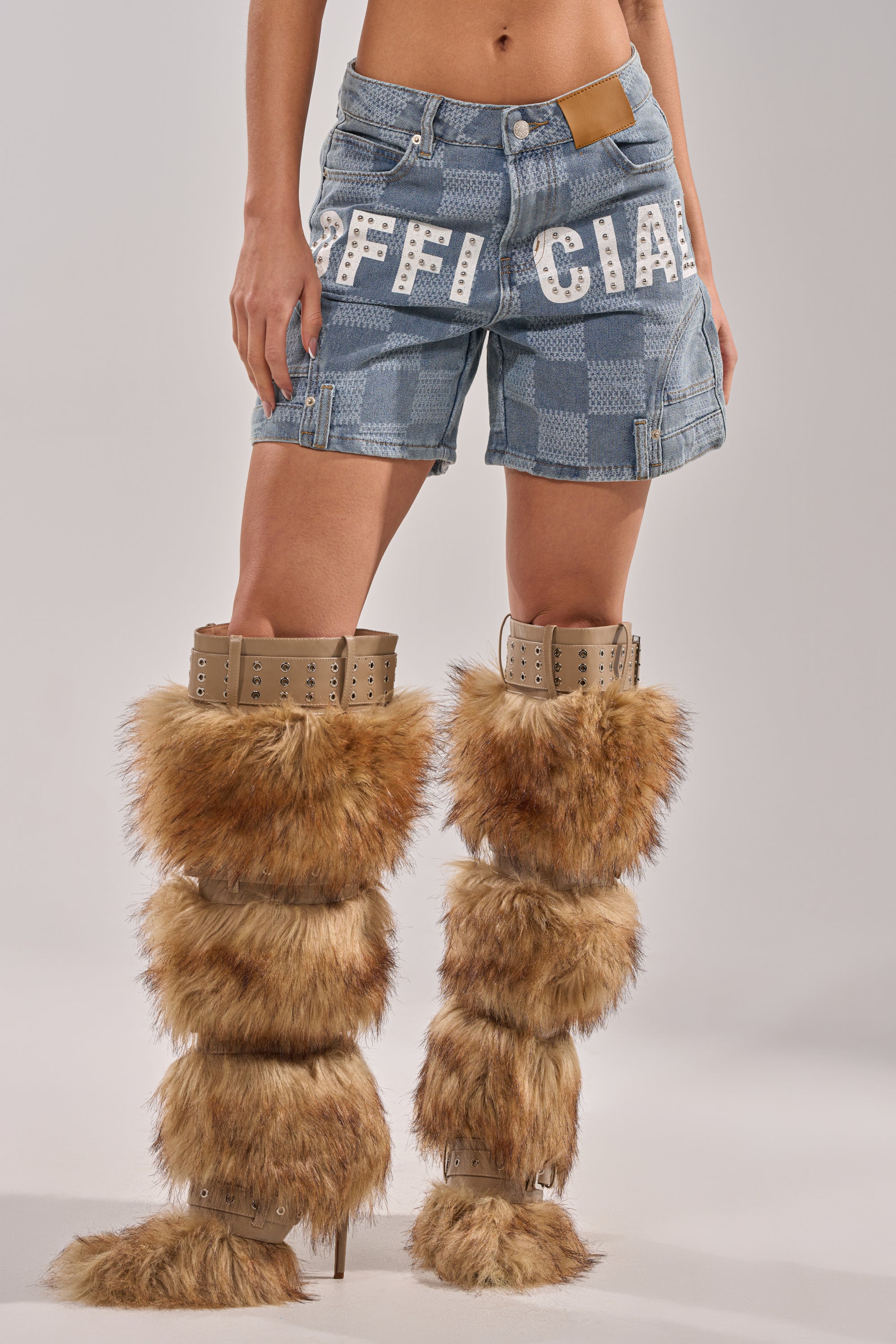 Someone stands confidently against a plain background, wearing OFFICIAL DENIM BERMUDA SHORTS—blue checkered, light-wash, with "OFFICIAL" text—and tall brown furry high-heeled boots featuring buckle details. 3