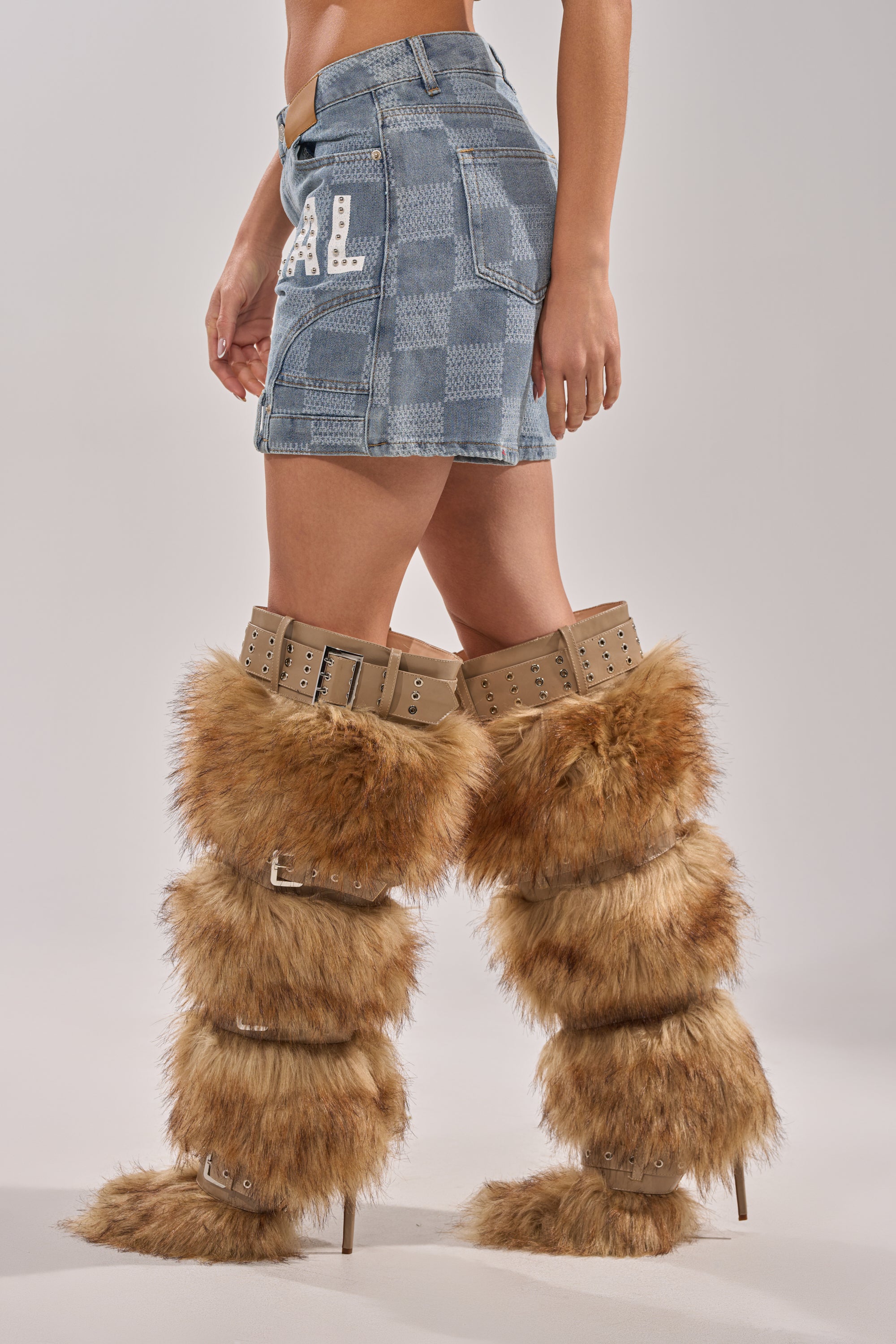 A person wearing the OFFICIAL DENIM BERMUDA SHORT and tall, furry, brown boots with multiple buckle straps stands against a plain, light background. 4