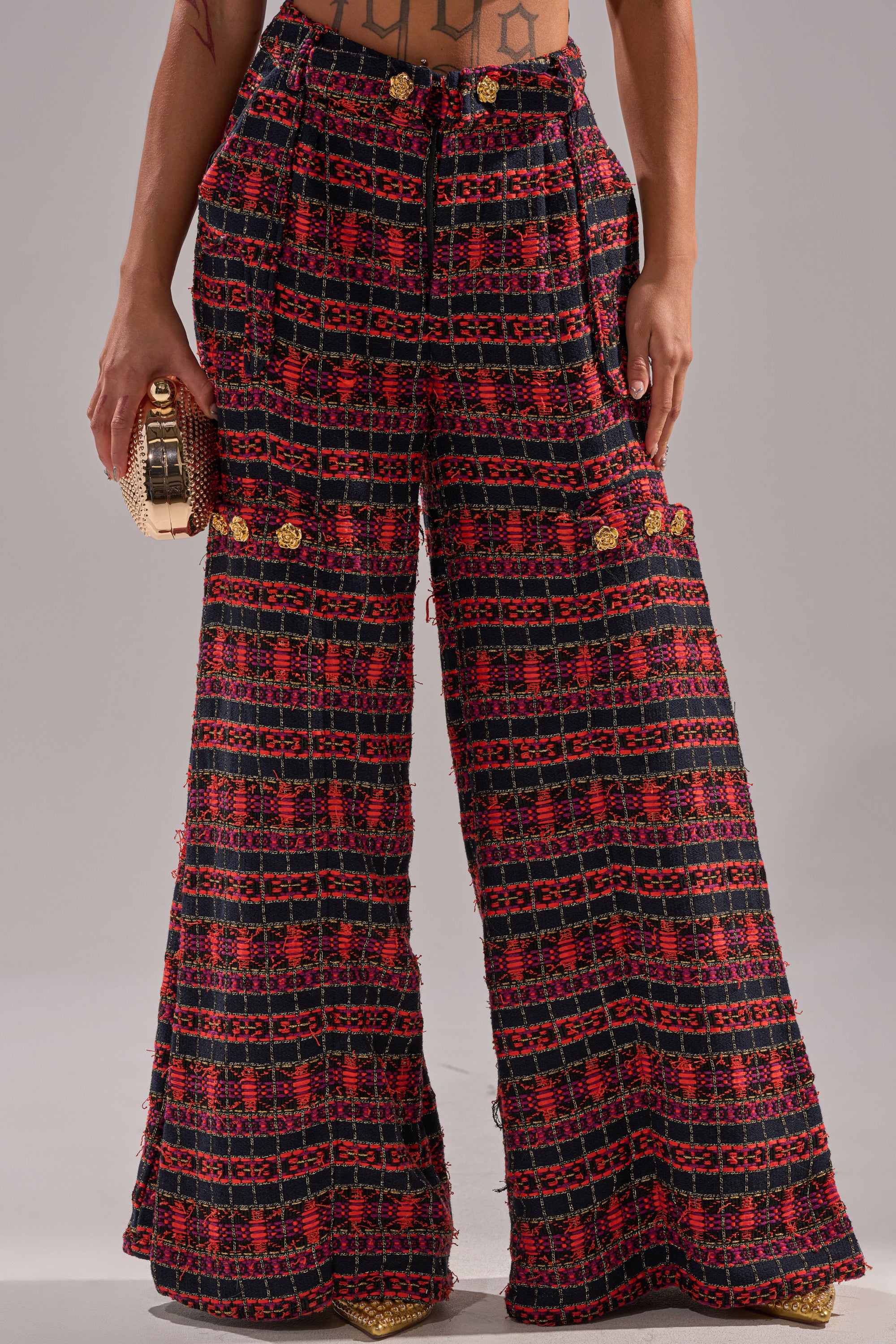 The ONLY THINK ABOUT YOU TROUSER IN TWEED features a high-waisted, vintage-inspired wide-leg design in red and black geometric pattern, paired with a textured gold clutch and pointed shoes. Only the lower torso and legs are shown. 1