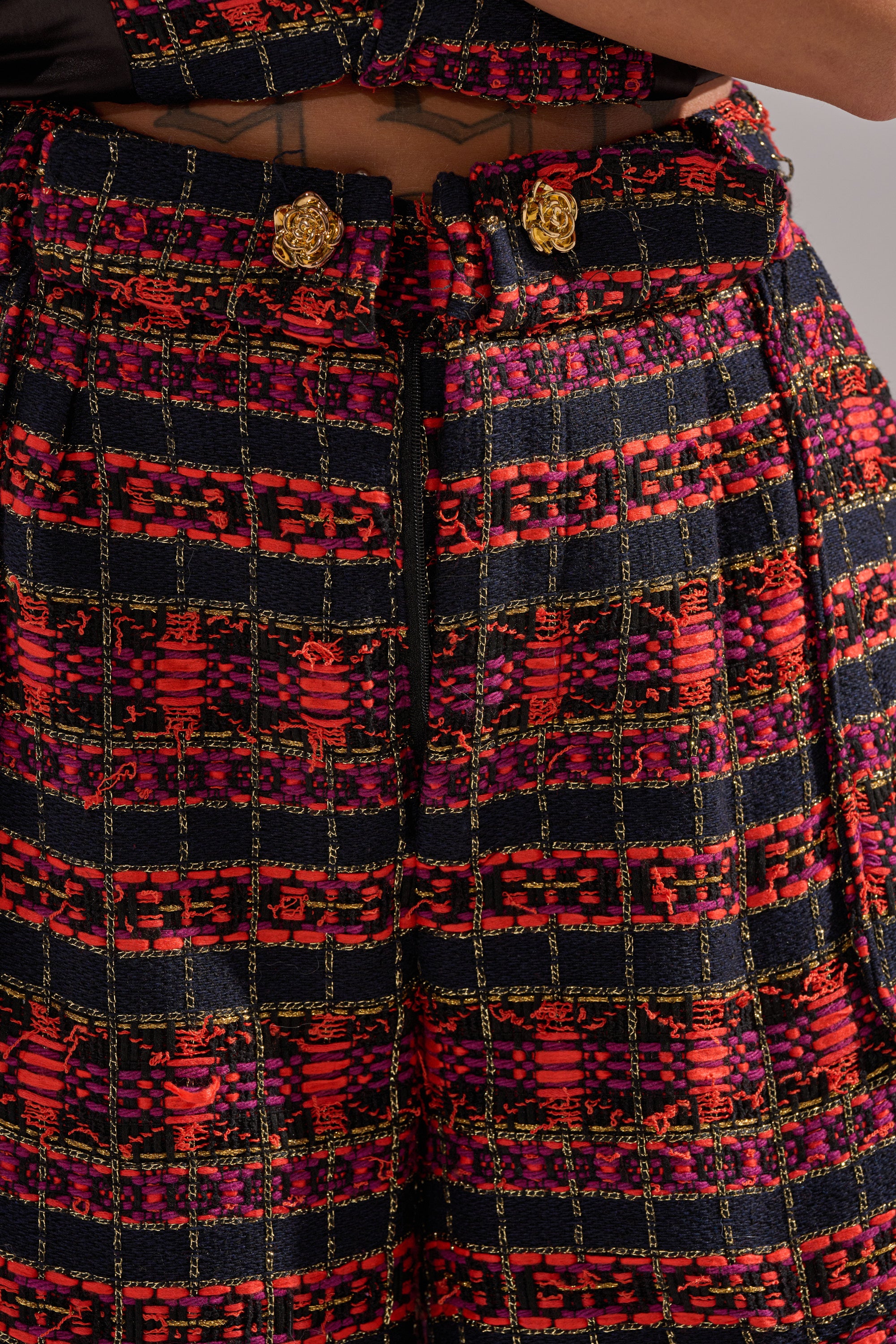 Close-up of ONLY THINK ABOUT YOU TROUSER IN TWEED, featuring a high waist, wide legs, bold red, pink, and black checkered tweed, gold decorative buttons, and a center zipper. 7