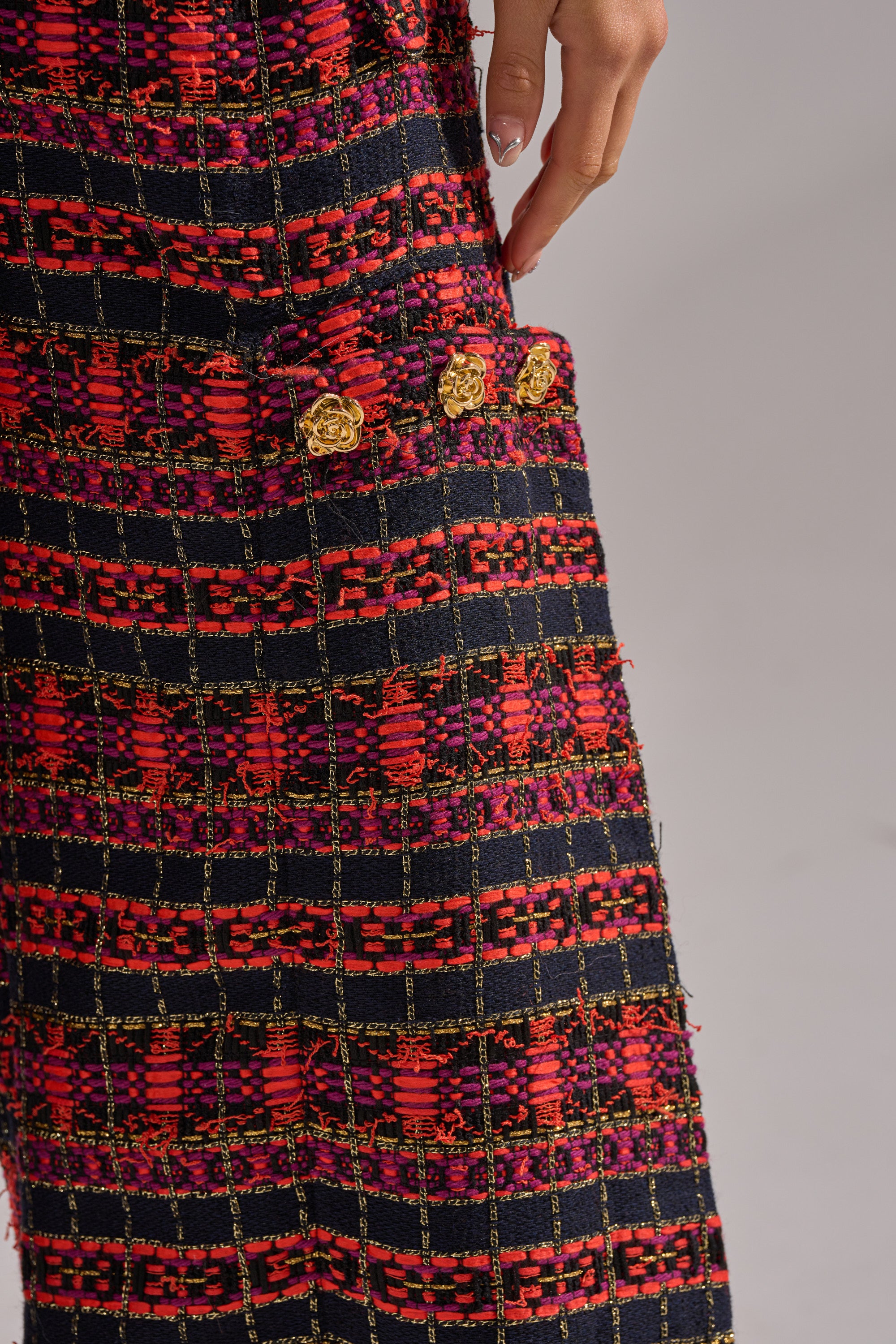 A hand rests on the pocket of the ONLY THINK ABOUT YOU TROUSER IN TWEED, featuring vintage-style textured fabric with a red, pink, and black checkered pattern and four gold decorative buttons. 8