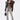A person wearing a black leather jacket, sheer black bralette, ULTRA DISTRESSED SKINNY DENIM jeans, high-heeled sandals, sunglasses, and holding a black handbag stands confidently against a plain white background.