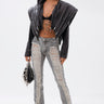 A person wearing a black leather jacket, sheer black bralette, ULTRA DISTRESSED SKINNY DENIM jeans, high-heeled sandals, sunglasses, and holding a black handbag stands confidently against a plain white background.