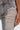 Close-up of a person wearing ULTRA DISTRESSED SKINNY DENIM in light grey with a high-rise waist, featuring extensive horizontal rips and frayed threads on the thigh. Their hand with nude nails rests near the ripped area.
