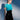 A woman with short brown hair stands against a blue and white background, wearing a fitted turquoise top, thigh-high patterned stockings, and the LETS DO BUSINESS MINI SKIRT. She looks confidently to the side with a soft shadow behind her.