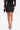 Woman wearing the THIS IS THE LIFE FAUX LEATHER MINI SKIRT, styled with a black lace long-sleeve top, black pointed heels with gold accents, and a black feather-detailed clutch, standing against a plain white background.